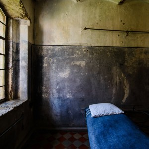 Kairėj pusėje – langas su grotomis. Pro jį ant aptrupėjusių kameros sienų krenta blausi šviesa. Netoli lango šalia sienos – paklotas kalėjimo gultas: mėlyna antklodė ir balta pagalvė.