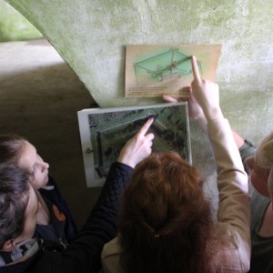 3 moksleivės ir 1 moksleivis lygina IX forto gynybinės sienos žemėlapį ir iš magnetinių plokštelių sudėliotą IX forto teritorijos vaizdą, nufotografuotą iš viršaus.